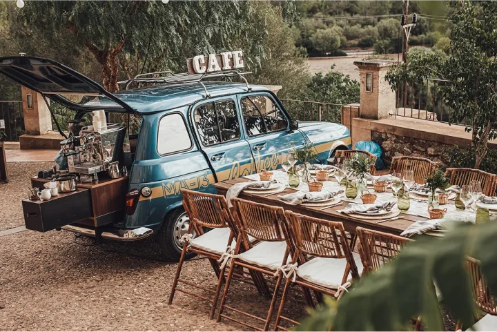 Outdoor event setup in Mallorca with a vintage coffee car bar and elegantly decorated dining table, showcasing seamless event management by a local Destination Management Company for the Balearic Islands. Balearic Elements DMC handles every detail including venues like beach clubs, fincas and bodegas, as well as decor, staffing, lighting, photography, video and live entertainment.